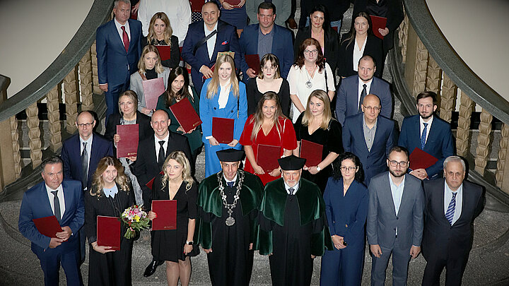 Zdjęcie grupowe absolwentów studiów podyplomowych stojących na schodach w budynku A0 z wyższej perspektywy